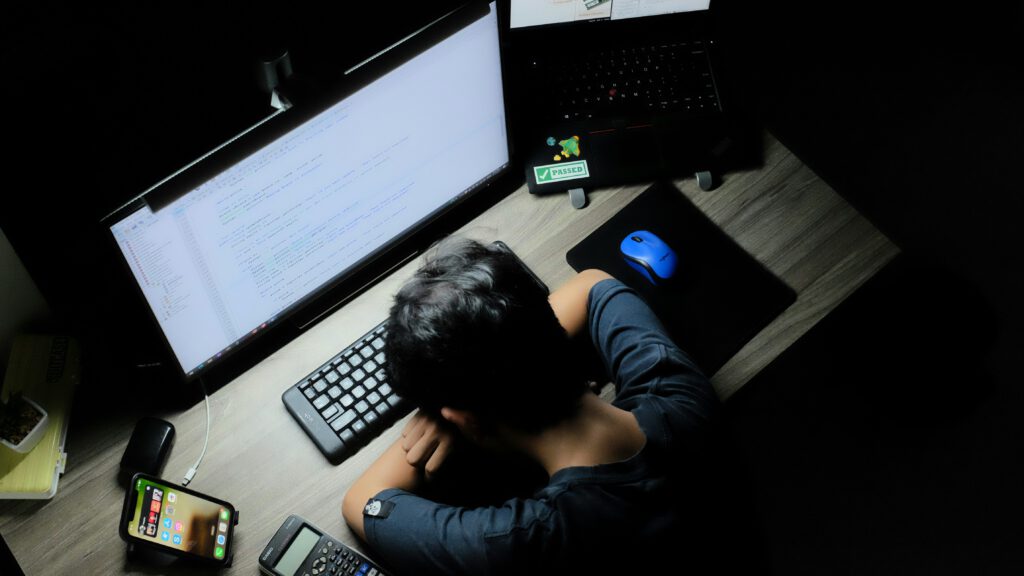 Ein junger Mensch, zusammengesackt vor Bildschirmen von Computern und Smartphones.